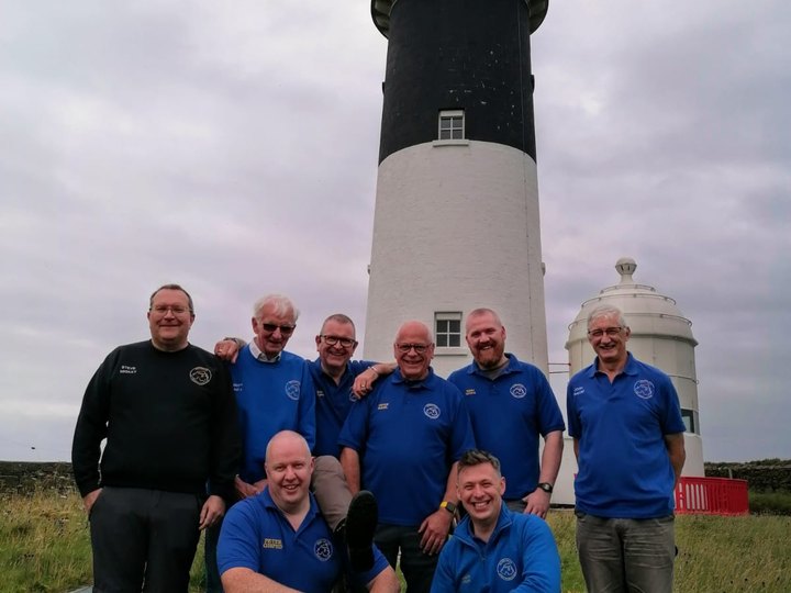 Club members gathered together beside a lighthouse.